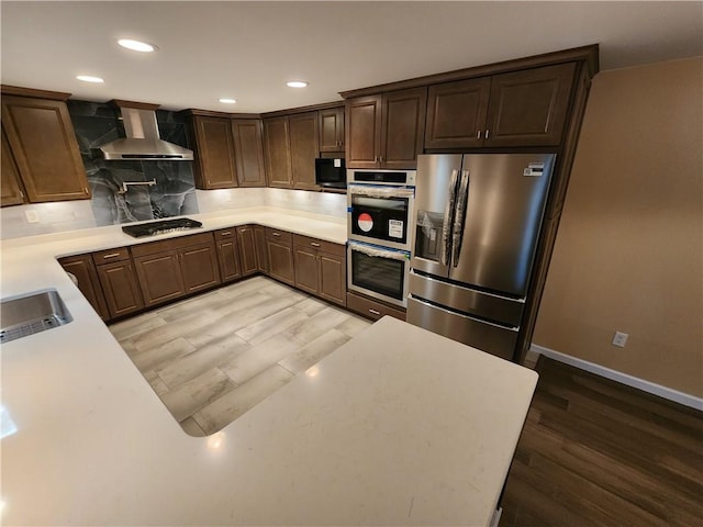 kitchen featuring appliances with stainless steel finishes, light countertops, a sink, and wall chimney exhaust hood