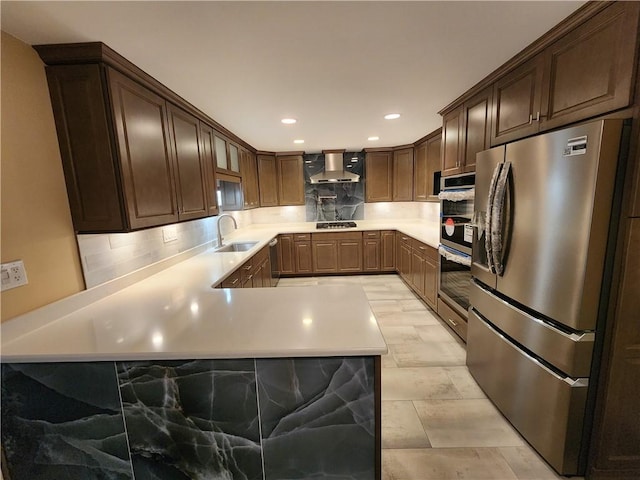 kitchen featuring stainless steel appliances, a sink, light countertops, wall chimney exhaust hood, and tasteful backsplash