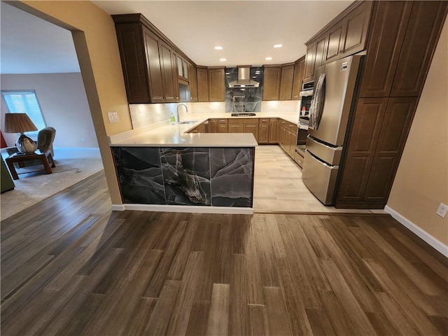 kitchen featuring wall chimney exhaust hood, stainless steel appliances, a sink, and light countertops