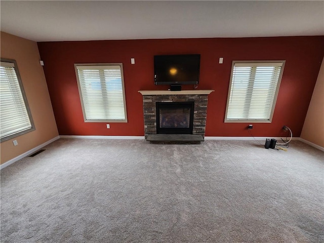 unfurnished living room featuring plenty of natural light, baseboards, visible vents, carpet flooring, and a fireplace