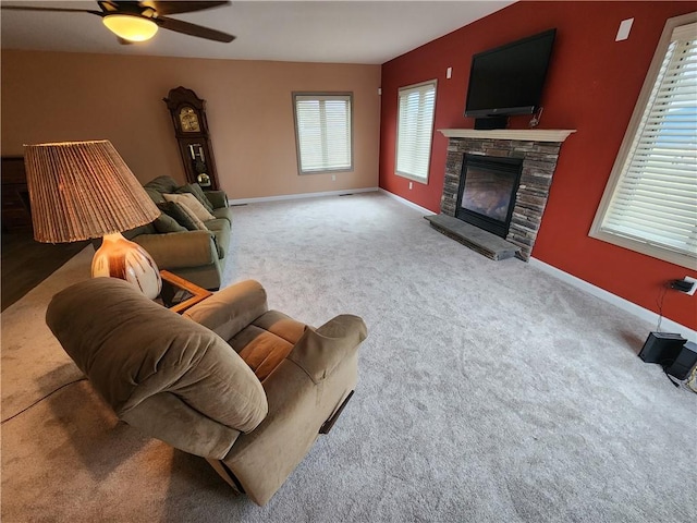 living room featuring a stone fireplace, carpet flooring, a ceiling fan, and baseboards