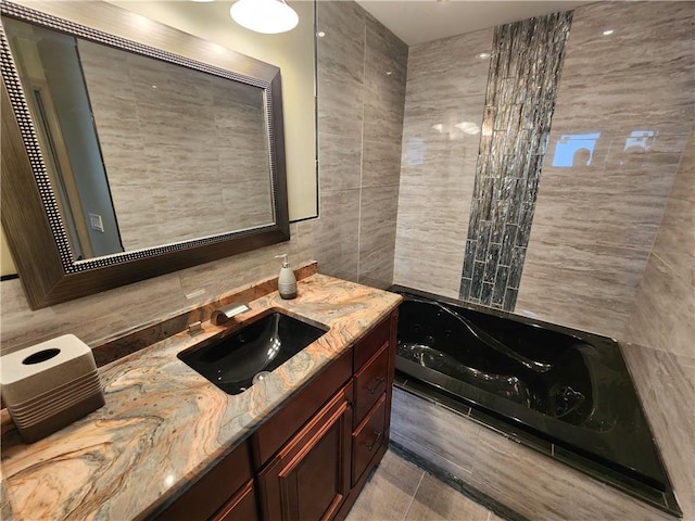 bathroom featuring tile patterned floors, tile walls, a tub with jets, and vanity