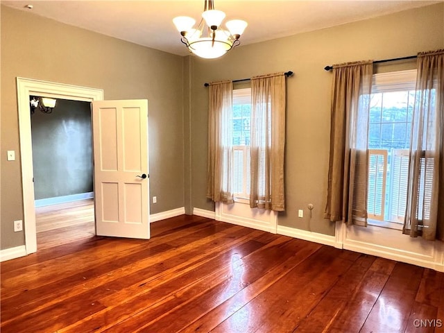 spare room featuring a chandelier, baseboards, and hardwood / wood-style floors