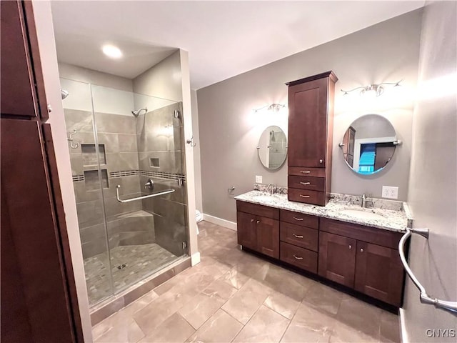 bathroom with double vanity, a stall shower, a sink, and baseboards