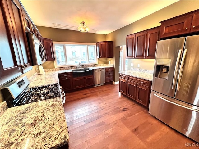 kitchen featuring a sink, appliances with stainless steel finishes, wood finished floors, and light stone countertops