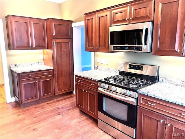 kitchen with appliances with stainless steel finishes, light wood-type flooring, and light stone countertops