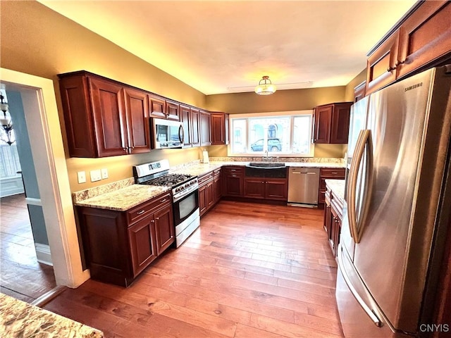 kitchen featuring stainless steel appliances, a sink, light wood-style flooring, and light stone countertops