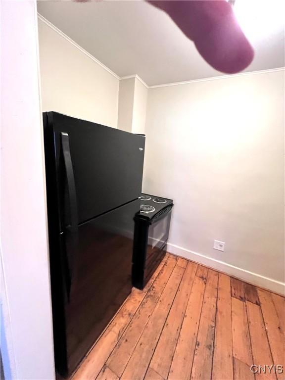 kitchen featuring black appliances, baseboards, light wood finished floors, and crown molding