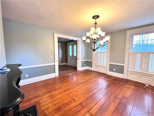 unfurnished dining area with a chandelier, wood-type flooring, and baseboards