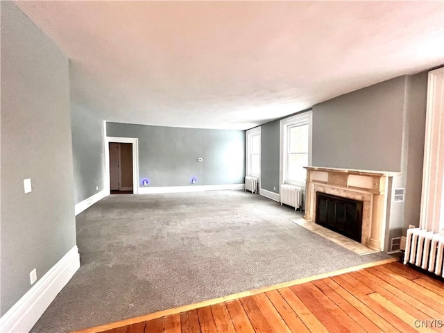 unfurnished living room featuring radiator, wood-type flooring, and a premium fireplace