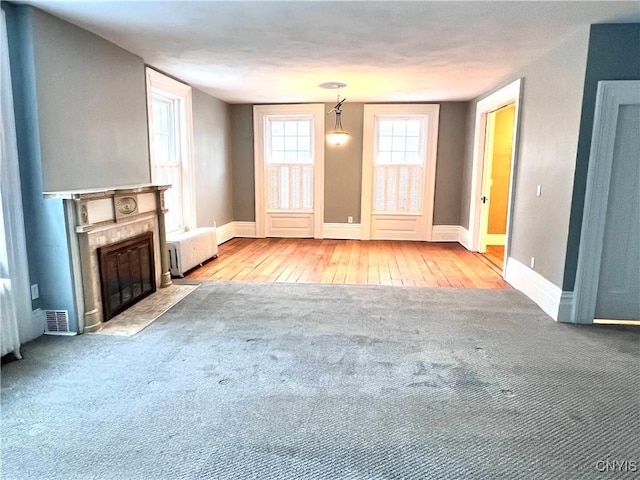 unfurnished living room with a premium fireplace, carpet flooring, visible vents, baseboards, and radiator