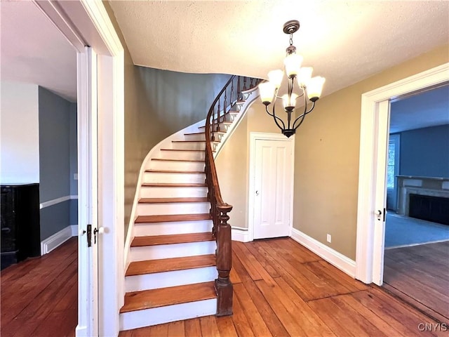 stairs featuring a chandelier, baseboards, a fireplace, and hardwood / wood-style floors