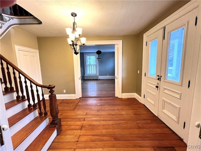 foyer with stairs, radiator, a chandelier, baseboards, and hardwood / wood-style flooring