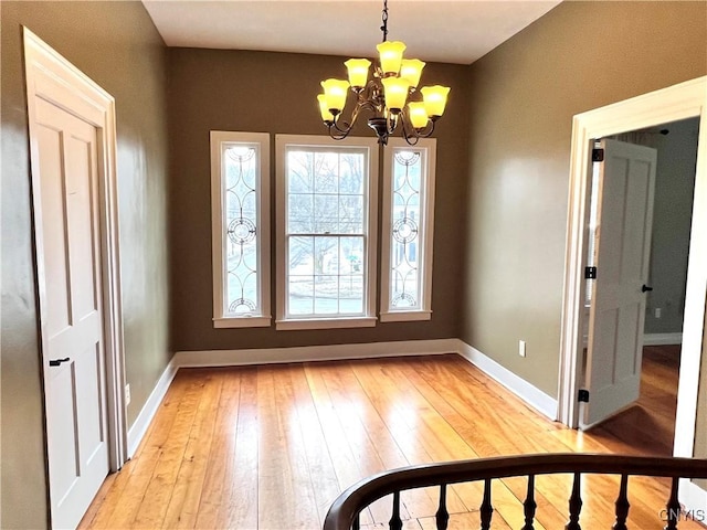 unfurnished dining area featuring light wood finished floors, baseboards, and a chandelier