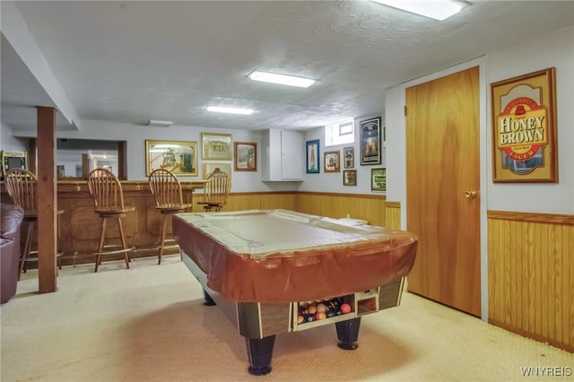 recreation room with a bar, wood walls, light carpet, and wainscoting