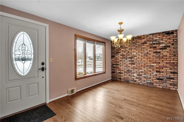 entrance foyer with visible vents, baseboards, brick wall, wood finished floors, and an inviting chandelier