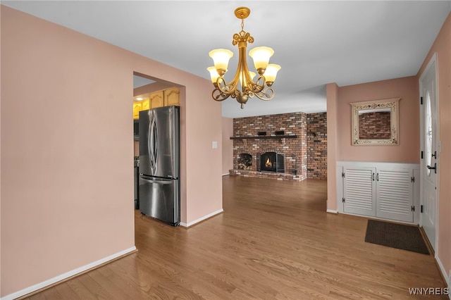 unfurnished dining area with a chandelier, a fireplace, baseboards, and wood finished floors