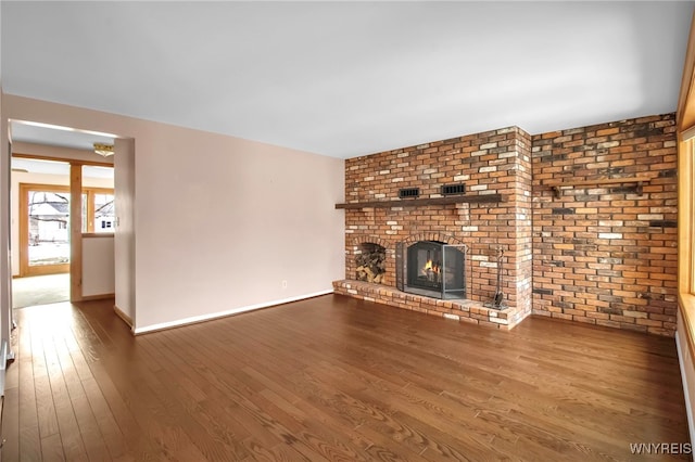 unfurnished living room with a brick fireplace, wood finished floors, and baseboards