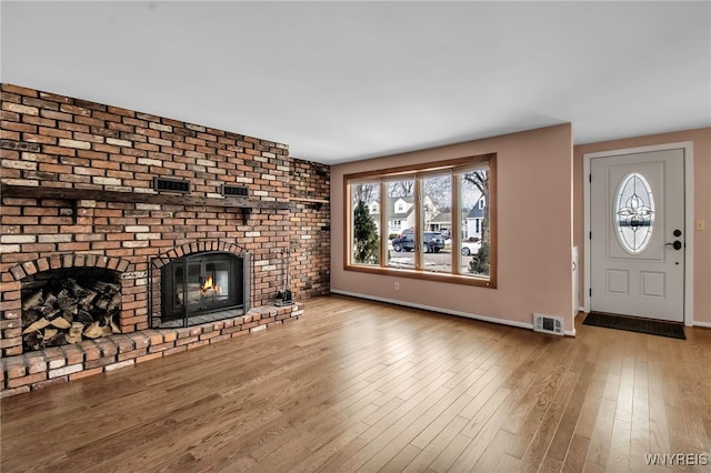 unfurnished living room featuring visible vents, a fireplace, baseboards, and wood finished floors