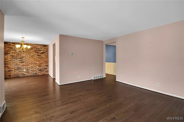 empty room featuring dark wood-type flooring, visible vents, brick wall, and an inviting chandelier