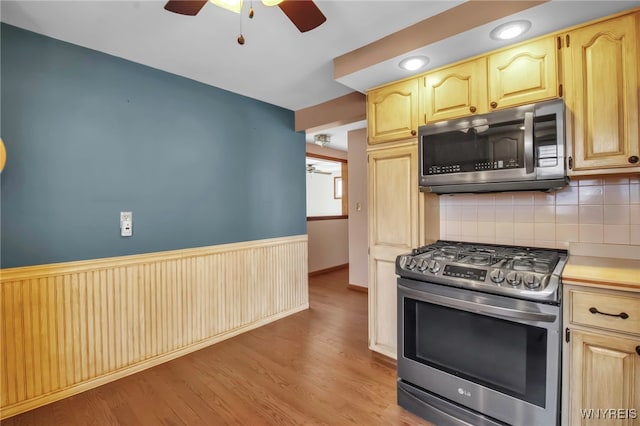 kitchen with light wood finished floors, a wainscoted wall, ceiling fan, appliances with stainless steel finishes, and light countertops