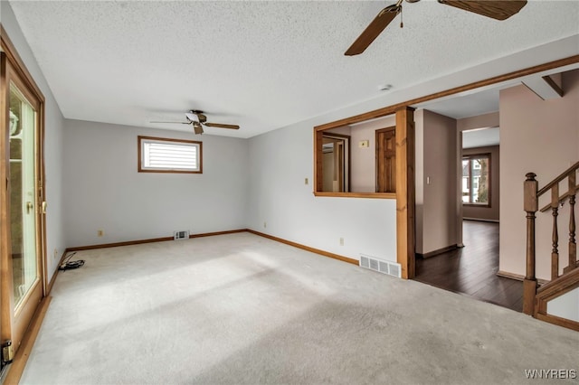 carpeted spare room featuring visible vents, ceiling fan, a textured ceiling, baseboards, and stairs