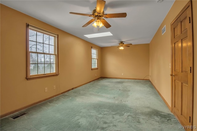 empty room with a skylight, carpet flooring, visible vents, and baseboards