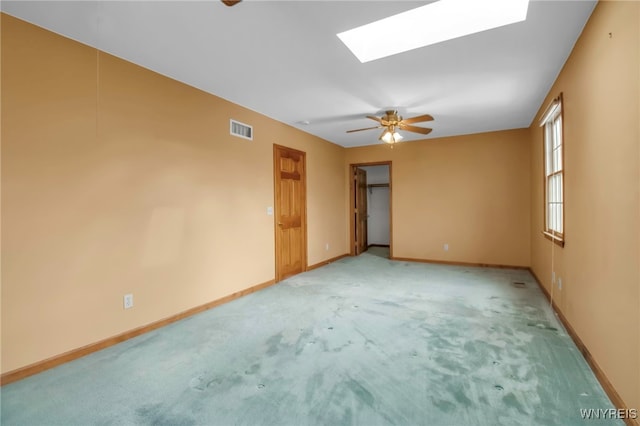 empty room featuring light carpet, a skylight, a ceiling fan, visible vents, and baseboards