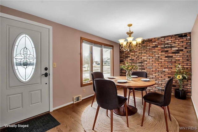 dining room with a notable chandelier, light wood finished floors, visible vents, brick wall, and baseboards