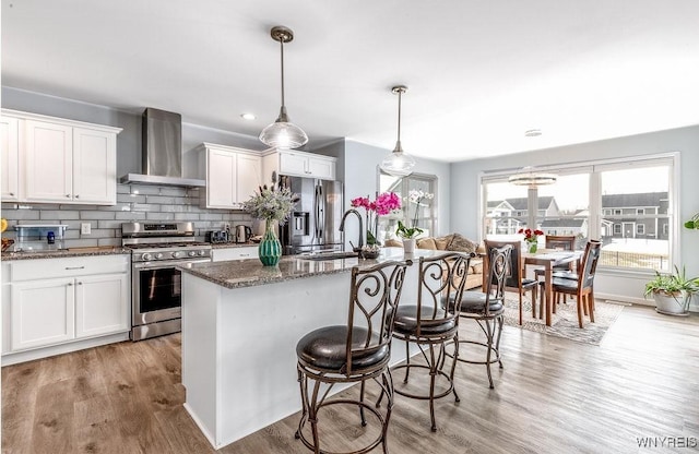 12 Kevwood Ln, Lancaster, NY 14086 - kitchen featuring a kitchen bar, appliances with stainless steel finishes, a sink, light wood finished floors, and wall chimney exhaust hood