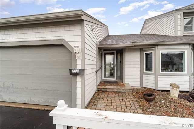 view of exterior entry with a shingled roof and an attached garage