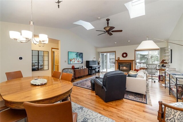 living area with ceiling fan with notable chandelier, lofted ceiling with skylight, a glass covered fireplace, and light wood-style flooring