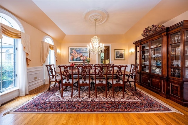 dining space featuring a chandelier, a decorative wall, wood finished floors, and wainscoting