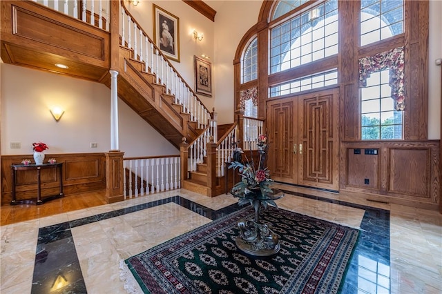 foyer featuring marble finish floor, wainscoting, stairway, and a high ceiling