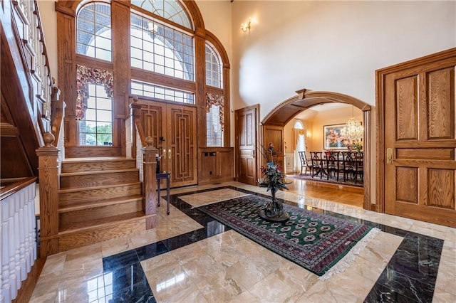 foyer with baseboards, arched walkways, marble finish floor, a high ceiling, and stairs