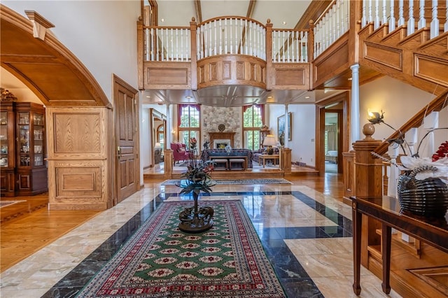 foyer entrance with a high ceiling, a fireplace, baseboards, stairway, and decorative columns