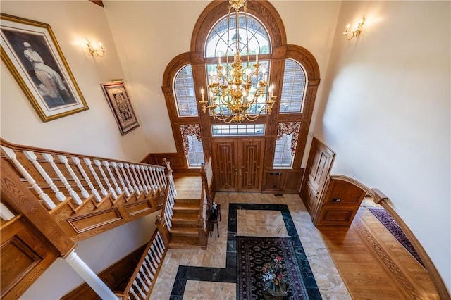 foyer entrance with arched walkways, stairway, a towering ceiling, wainscoting, and a chandelier