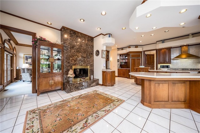 kitchen featuring wall chimney range hood, light tile patterned flooring, a high end fireplace, and decorative backsplash