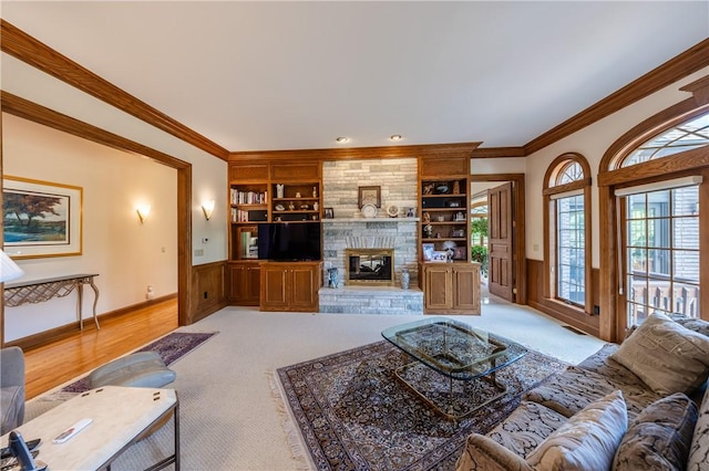 living area featuring a stone fireplace, built in features, wainscoting, carpet, and crown molding