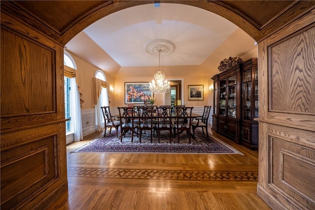 unfurnished dining area with a chandelier, arched walkways, wainscoting, and a decorative wall