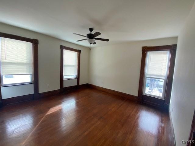 empty room with a wealth of natural light, dark wood-style flooring, ceiling fan, and baseboards