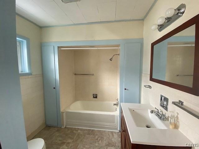 bathroom with toilet, washtub / shower combination, tile walls, and vanity