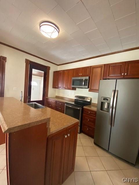 kitchen with a kitchen island with sink, stainless steel appliances, crown molding, a sink, and light tile patterned flooring