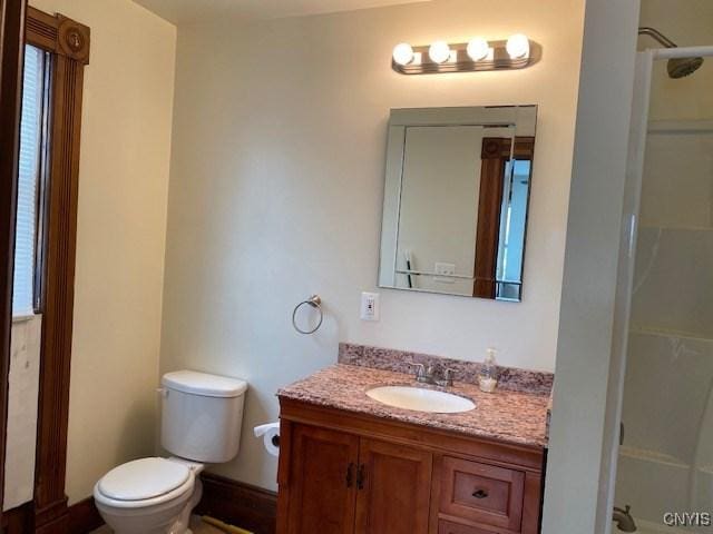 bathroom featuring baseboards, vanity, toilet, and walk in shower