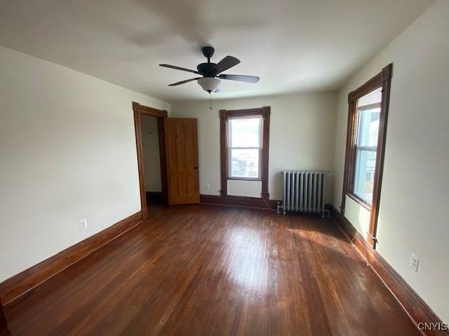 unfurnished room with radiator, a healthy amount of sunlight, baseboards, and dark wood finished floors