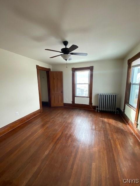 unfurnished room featuring baseboards, dark wood-type flooring, radiator heating unit, and a healthy amount of sunlight