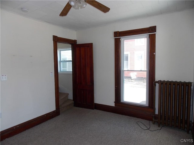 carpeted spare room with baseboards, stairway, a ceiling fan, and radiator