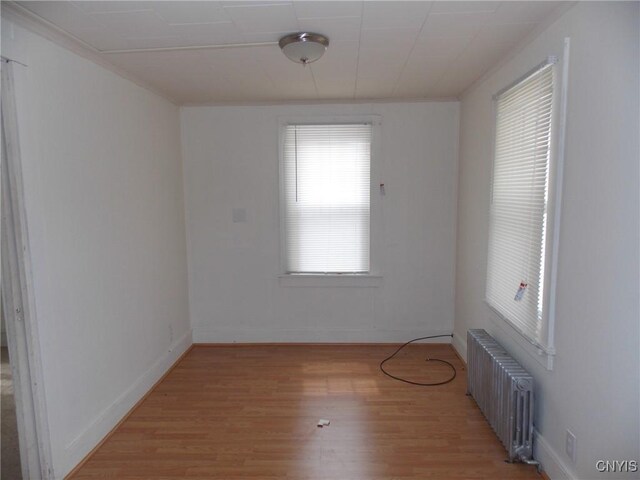 empty room with radiator, light wood-type flooring, and baseboards