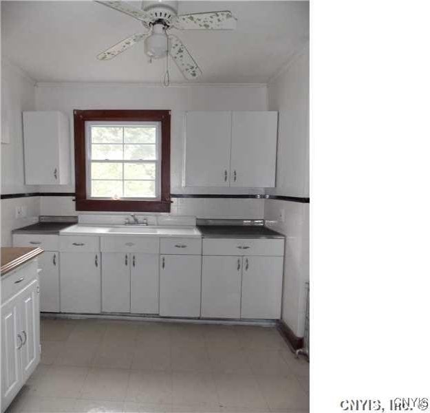 kitchen featuring ornamental molding, white cabinets, ceiling fan, and a sink