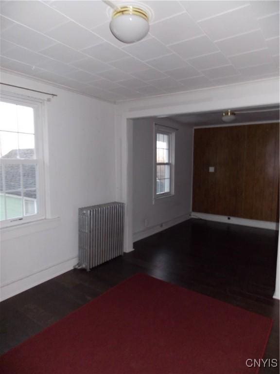 unfurnished room featuring a wealth of natural light, dark wood-style flooring, and radiator heating unit